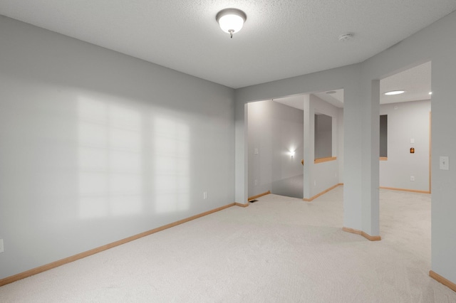 unfurnished room with light colored carpet, a textured ceiling, and baseboards