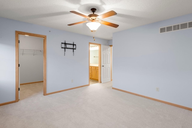 unfurnished bedroom featuring a textured ceiling, a spacious closet, visible vents, and baseboards