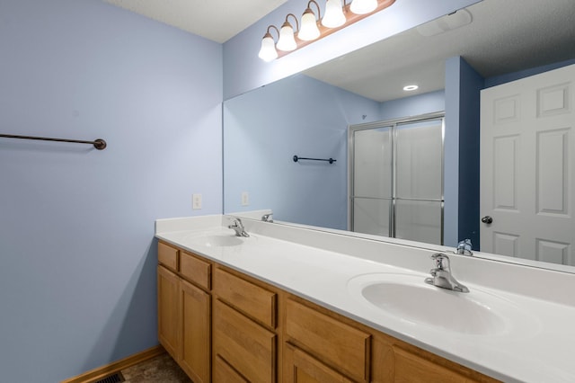 full bath with double vanity, a sink, a shower with shower door, and baseboards