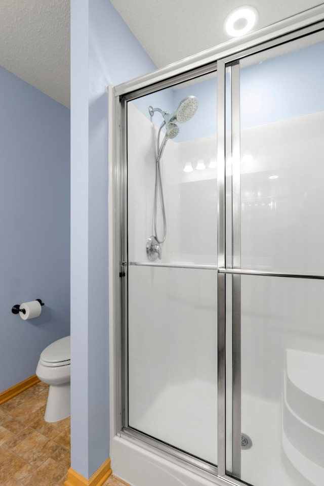 bathroom with a textured ceiling, a stall shower, toilet, and baseboards