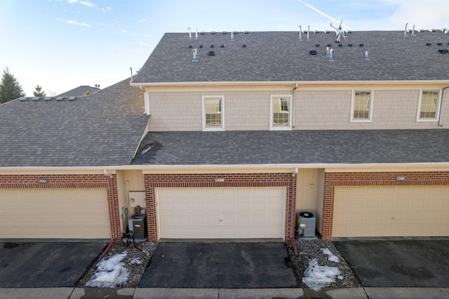 townhome / multi-family property with brick siding, central AC unit, aphalt driveway, and roof with shingles