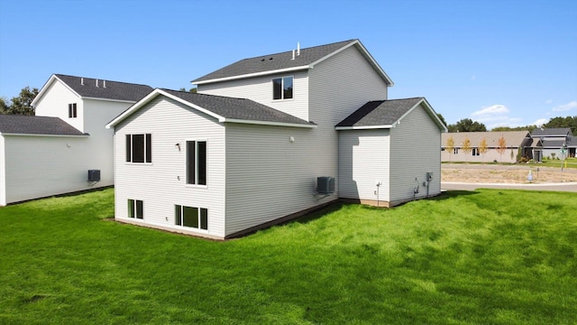 rear view of house with central air condition unit and a lawn