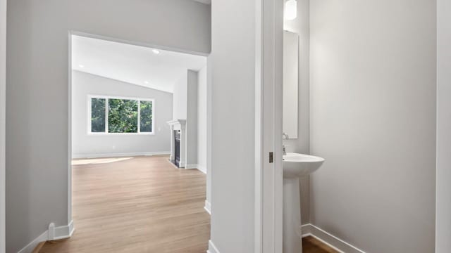 hallway featuring light hardwood / wood-style floors, lofted ceiling, and sink