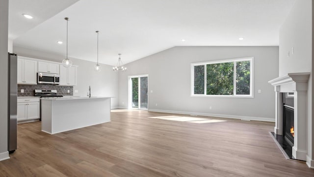 kitchen with stainless steel appliances, tasteful backsplash, decorative light fixtures, a kitchen island with sink, and white cabinets