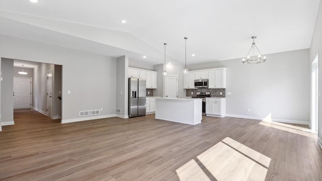 kitchen featuring hanging light fixtures, stainless steel appliances, an island with sink, vaulted ceiling, and white cabinets