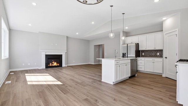 kitchen featuring white cabinetry, tasteful backsplash, pendant lighting, lofted ceiling, and a center island with sink