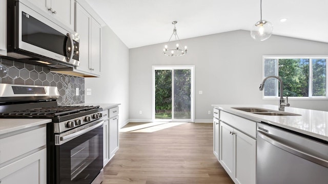 kitchen with appliances with stainless steel finishes, tasteful backsplash, sink, white cabinetry, and lofted ceiling