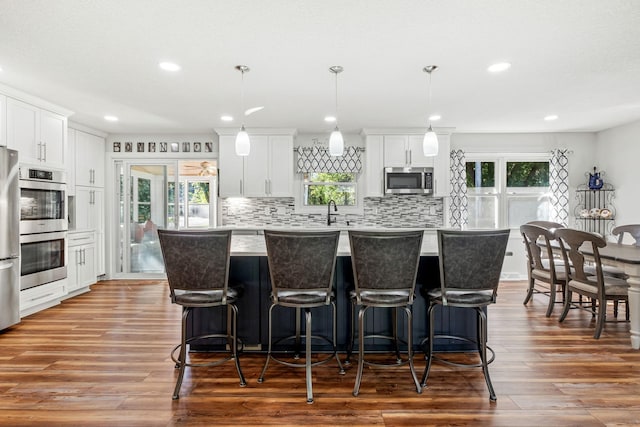 kitchen featuring white cabinetry, wood-type flooring, a center island, appliances with stainless steel finishes, and pendant lighting