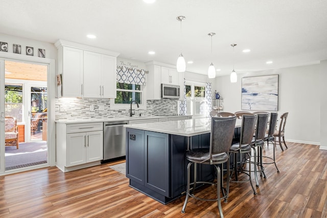 kitchen with white cabinetry, appliances with stainless steel finishes, a kitchen island, pendant lighting, and decorative backsplash