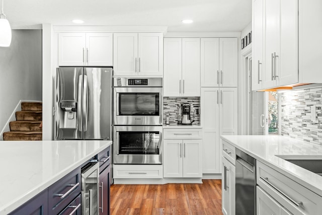 kitchen featuring appliances with stainless steel finishes, decorative light fixtures, wine cooler, white cabinets, and light stone counters