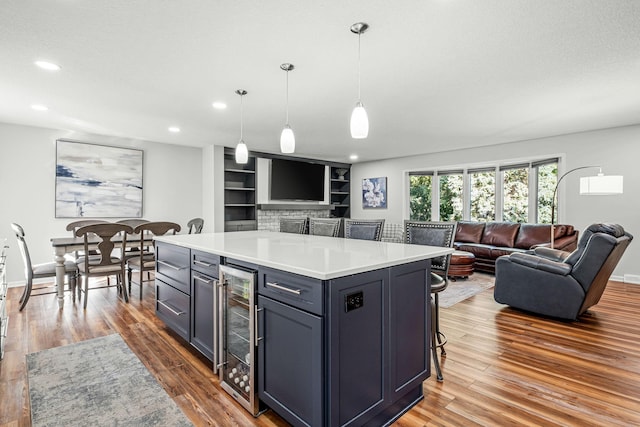 kitchen with a kitchen bar, a center island, hanging light fixtures, hardwood / wood-style flooring, and beverage cooler