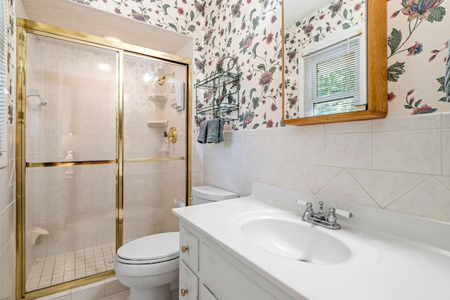 bathroom with vanity, toilet, a shower with door, and tile walls