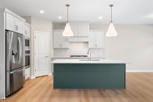 kitchen featuring appliances with stainless steel finishes, decorative light fixtures, sink, white cabinets, and a kitchen island with sink