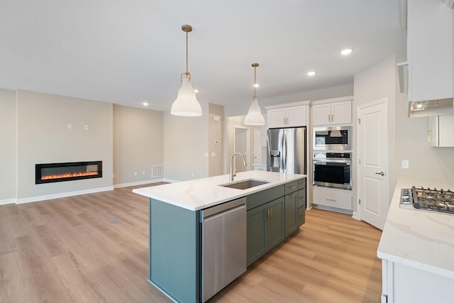 kitchen featuring sink, appliances with stainless steel finishes, a kitchen island with sink, hanging light fixtures, and white cabinets