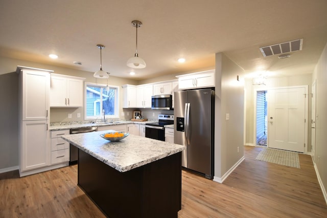 kitchen with stainless steel appliances, sink, white cabinets, a kitchen island, and hanging light fixtures