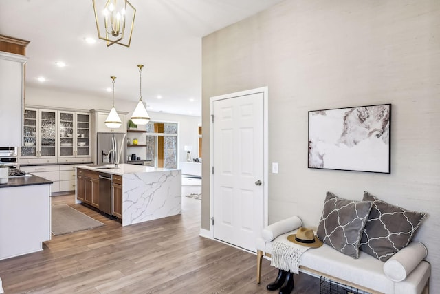 kitchen with stainless steel appliances, light stone counters, light hardwood / wood-style floors, decorative light fixtures, and a kitchen island with sink