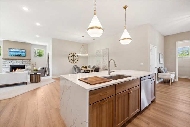 kitchen featuring pendant lighting, a stone fireplace, sink, stainless steel dishwasher, and an island with sink