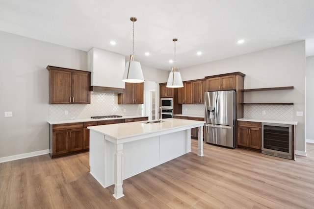 kitchen featuring premium range hood, a breakfast bar, an island with sink, beverage cooler, and stainless steel appliances