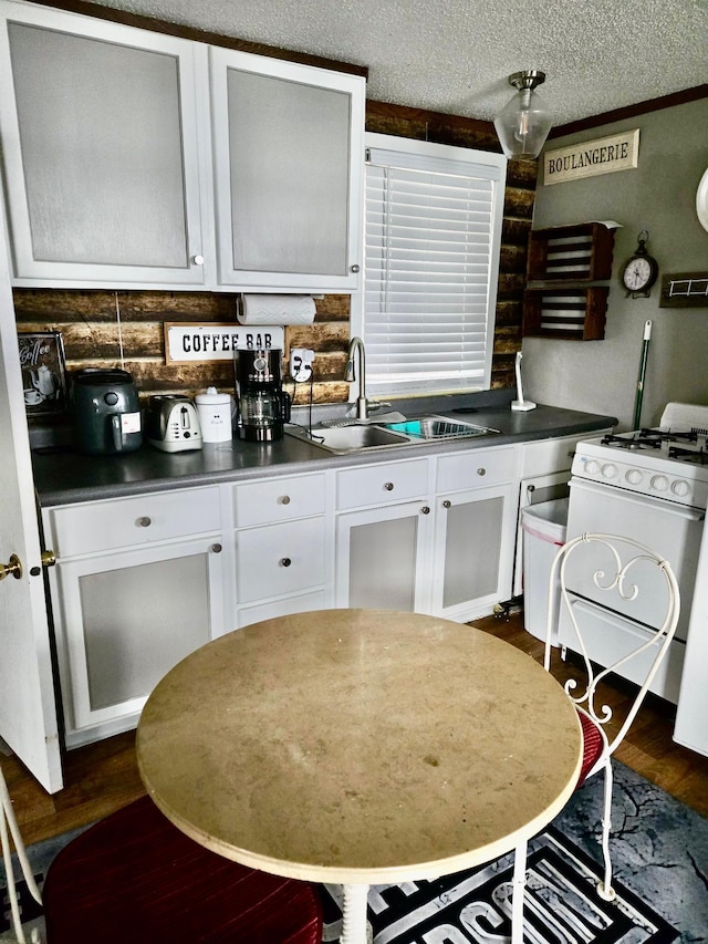 kitchen featuring gas range gas stove, a textured ceiling, dark wood-type flooring, sink, and white cabinets