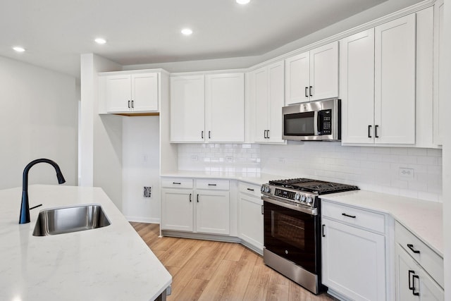 kitchen featuring backsplash, white cabinets, sink, light stone countertops, and appliances with stainless steel finishes