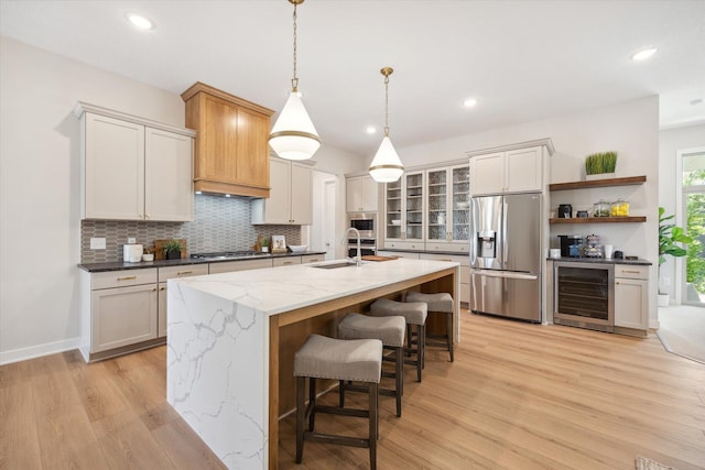 kitchen with sink, beverage cooler, stainless steel appliances, decorative light fixtures, and a center island with sink