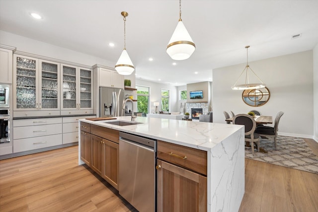 kitchen featuring appliances with stainless steel finishes, a kitchen island with sink, white cabinetry, hanging light fixtures, and a stone fireplace