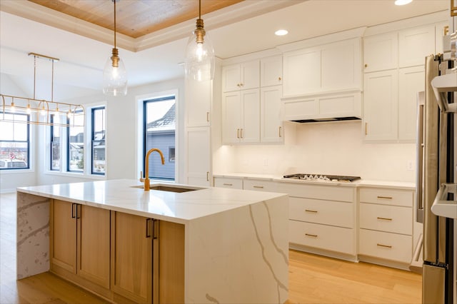 kitchen featuring a kitchen island with sink, light stone counters, white cabinetry, and decorative light fixtures