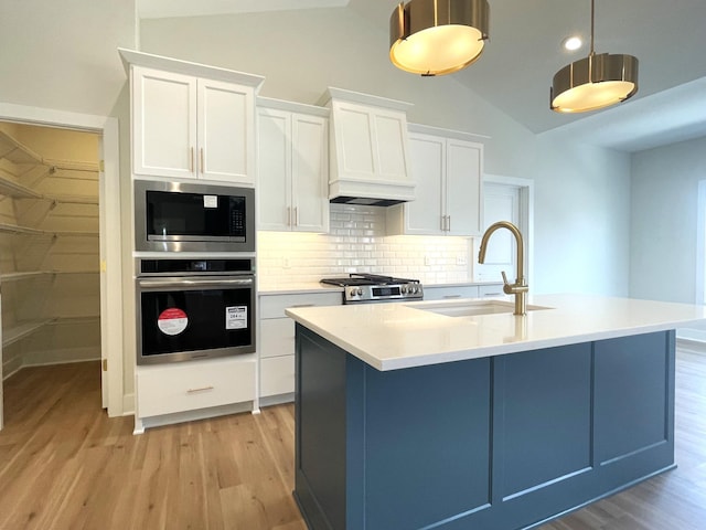 kitchen with custom exhaust hood, light wood-style floors, appliances with stainless steel finishes, and a sink