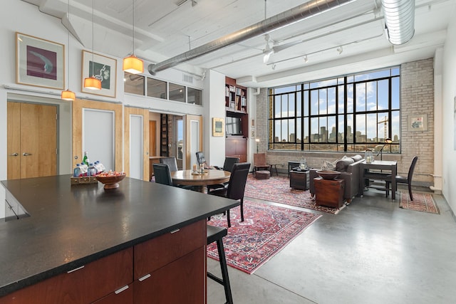 kitchen featuring concrete flooring, brick wall, a kitchen bar, a high ceiling, and hanging light fixtures