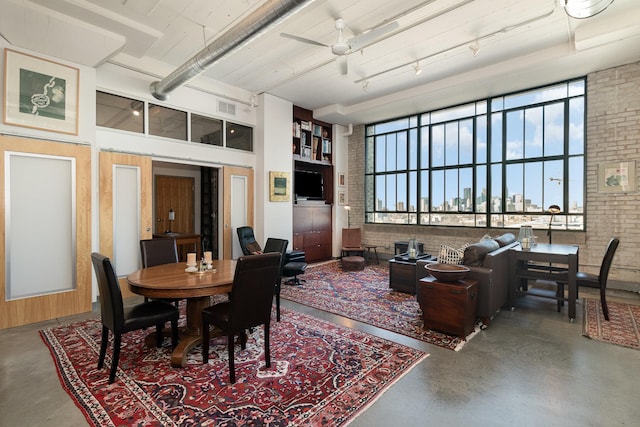 dining space with a towering ceiling, brick wall, concrete floors, and a wealth of natural light