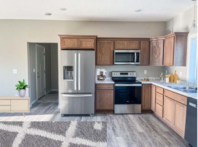 kitchen with stainless steel appliances, hanging light fixtures, sink, and light hardwood / wood-style flooring