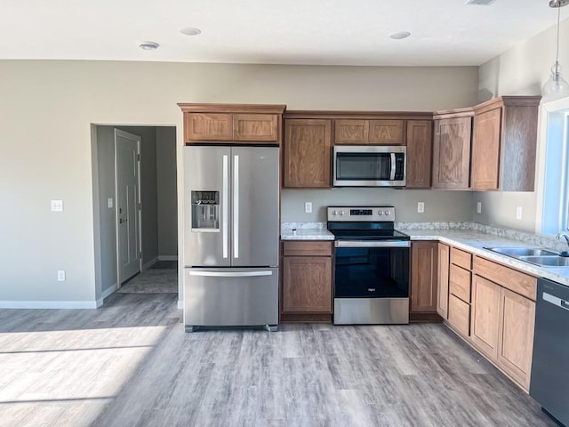 kitchen featuring appliances with stainless steel finishes, sink, hanging light fixtures, and light hardwood / wood-style flooring