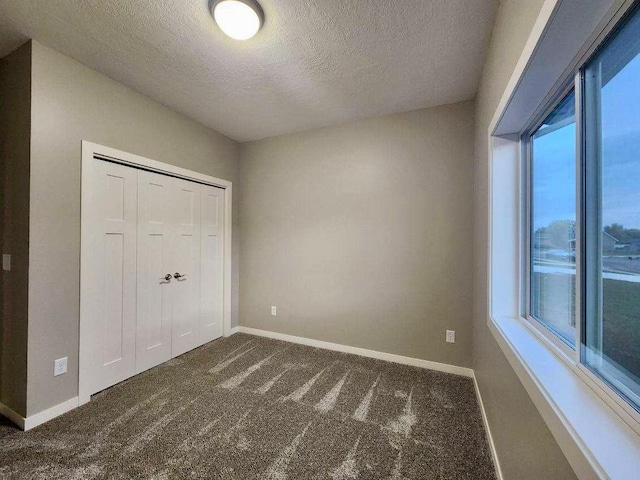 unfurnished bedroom featuring dark carpet, a closet, and a textured ceiling