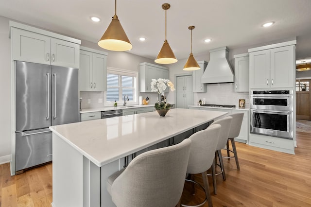 kitchen with appliances with stainless steel finishes, backsplash, premium range hood, sink, and a kitchen island