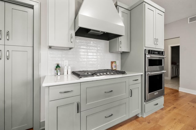 kitchen featuring appliances with stainless steel finishes, tasteful backsplash, light hardwood / wood-style flooring, and custom exhaust hood