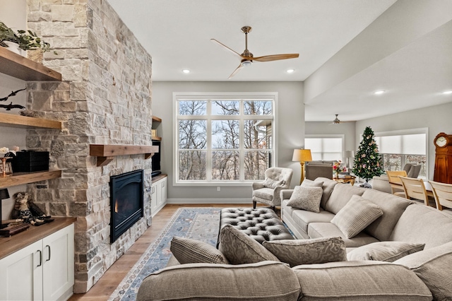 living room with light hardwood / wood-style floors, a stone fireplace, and ceiling fan