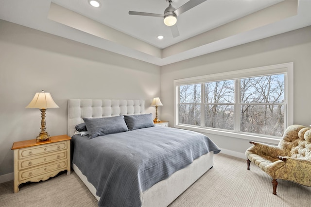 bedroom with ceiling fan, light colored carpet, and a tray ceiling