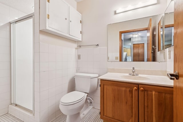 bathroom featuring tile patterned floors, toilet, a shower with shower door, tile walls, and vanity