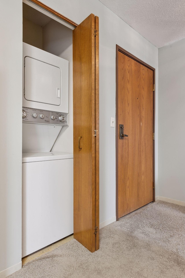 clothes washing area featuring light carpet, a textured ceiling, and stacked washing maching and dryer