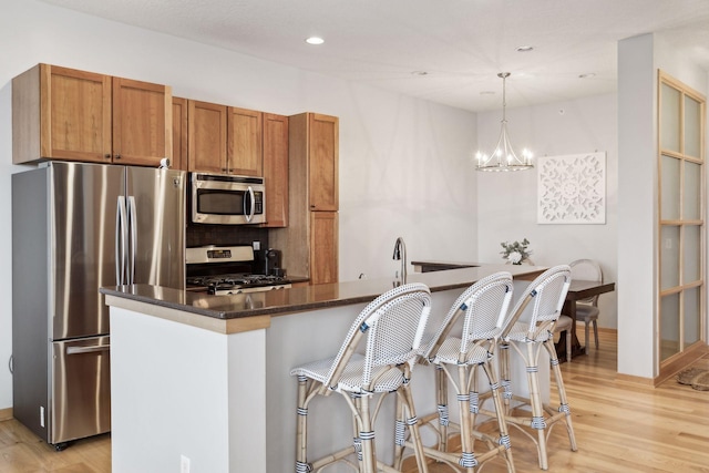 kitchen with dark stone countertops, appliances with stainless steel finishes, brown cabinets, light wood-style floors, and pendant lighting