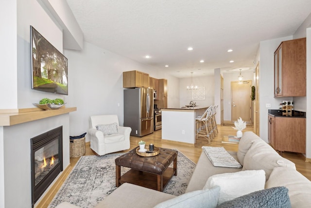 living room with light wood finished floors, a glass covered fireplace, a chandelier, and recessed lighting