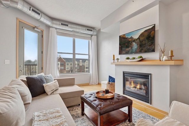 living area with baseboards, a textured ceiling, and a glass covered fireplace