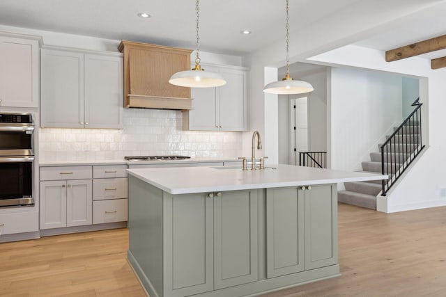 kitchen featuring an island with sink, appliances with stainless steel finishes, light countertops, pendant lighting, and a sink