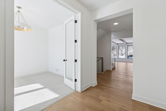 hall with light wood-type flooring, baseboards, and an upstairs landing