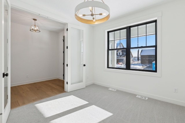 spare room with visible vents, baseboards, a notable chandelier, and light colored carpet