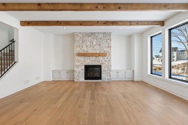 unfurnished living room featuring stairway, light wood-type flooring, a stone fireplace, and baseboards