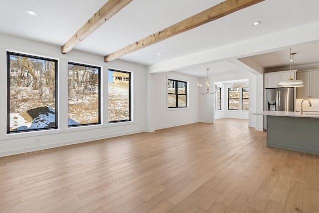 unfurnished living room with light wood-style flooring, recessed lighting, a notable chandelier, baseboards, and beam ceiling