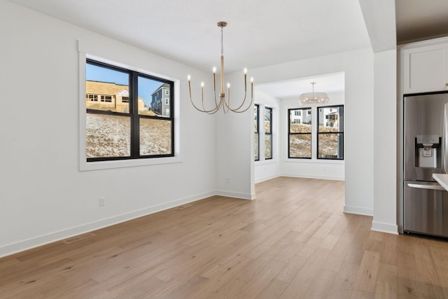 unfurnished dining area with a wealth of natural light, light wood-type flooring, a chandelier, and visible vents