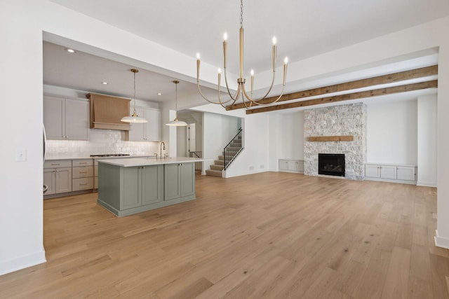 kitchen with open floor plan, light countertops, tasteful backsplash, an island with sink, and decorative light fixtures