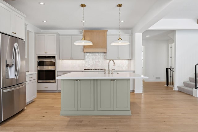 kitchen with white cabinets, decorative light fixtures, a kitchen island with sink, stainless steel appliances, and light countertops